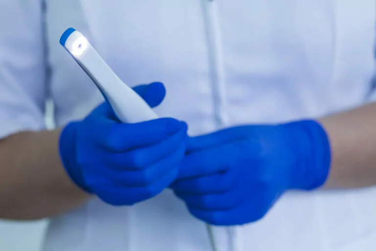 Dentist in blue gloves holding an intraoral camera tool in both hands